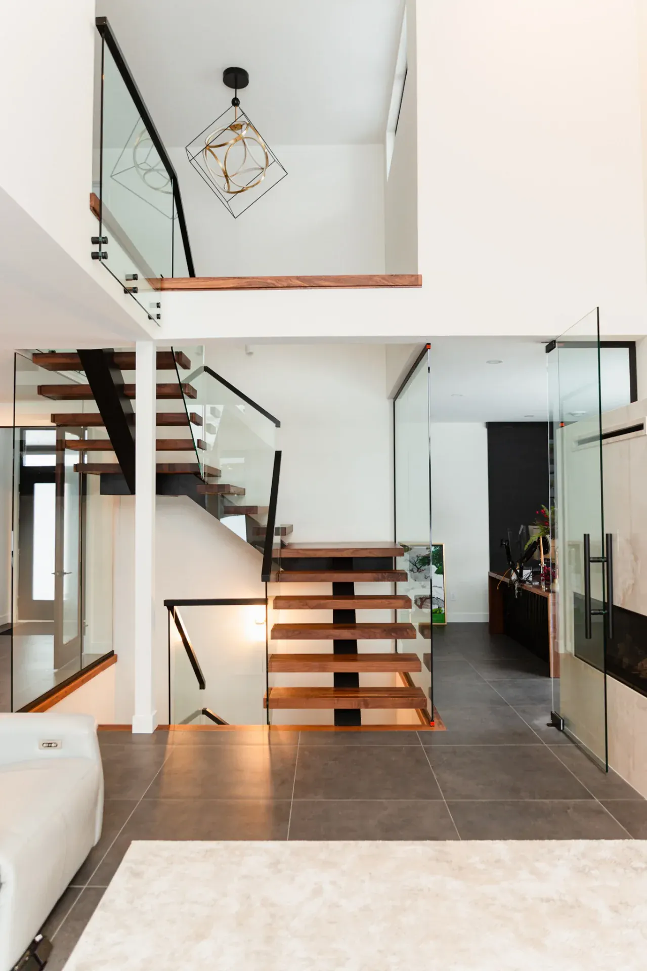 Escalier en noyer massif double volée, limon central acier noir et garde-corps verre, luminaire design suspendu