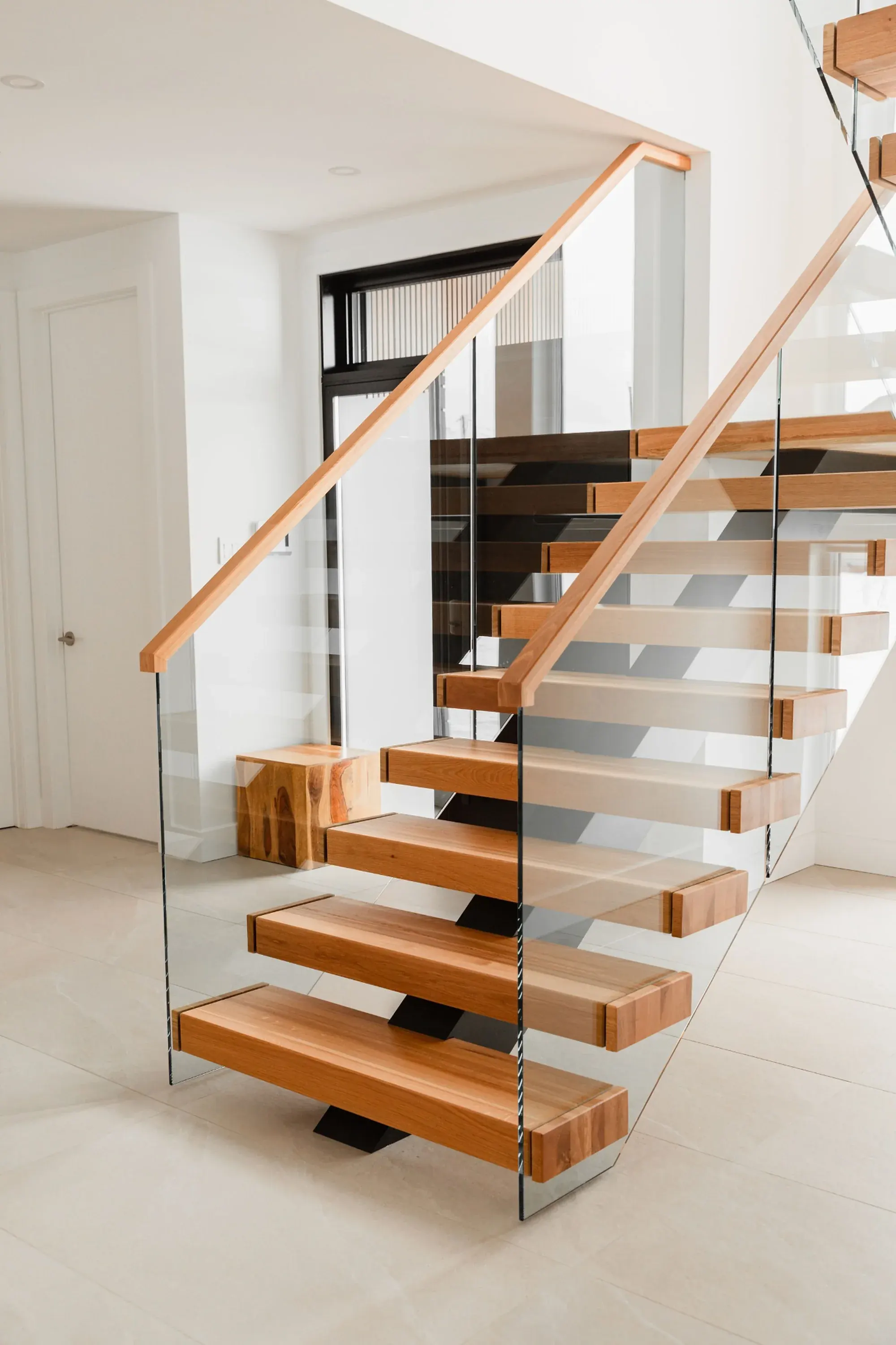 Escalier en noyer massif vue plongeante, garde-corps verre fumé et rampe acier noir, résidence haut de gamme