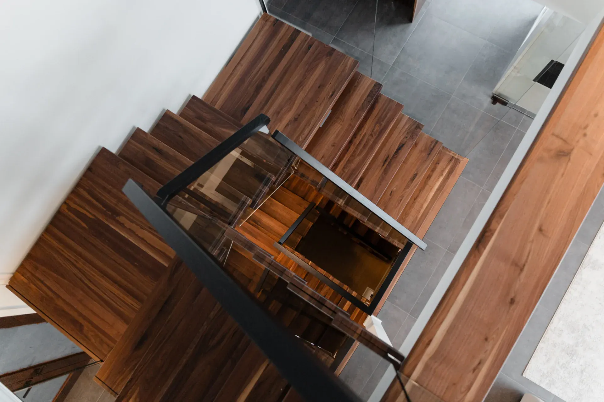 Escalier en noyer massif ouvert sur salon et salle à manger, limon central acier noir et garde-corps verre, demeure contemporaine