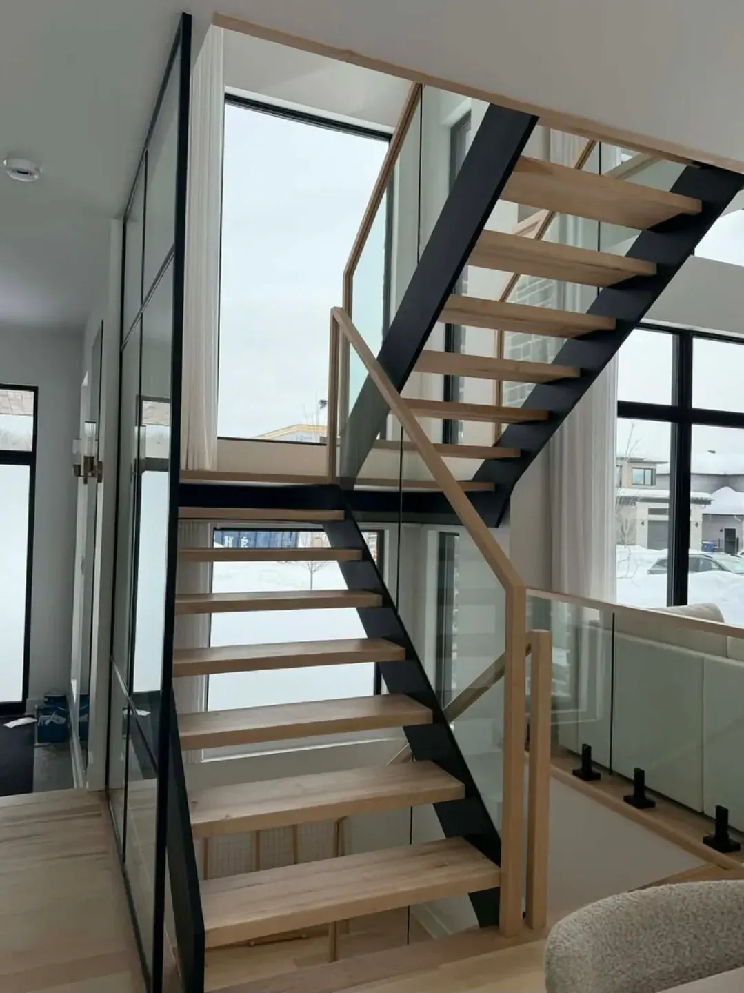 Escalier en noyer massif vue plongeante, marches larges et garde-corps verre fumé, résidence Grand Montréal